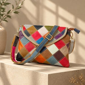 Puede incluir: Un bolso bandolera rectangular con un diseño de patchwork multicolor con paneles de cuero en forma de diamante en rojo, azul, verde, marrón y blanco. El bolso incluye una solapa plegable, una hebilla de metal dorado y una correa ajustable.
