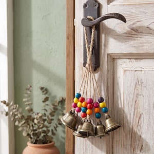 May include: A decorative hanging ornament featuring five brass-coloured metal bells suspended by natural jute twine. Each twine strand is accented with a series of colourful wooden beads in shades of blue, yellow, red, pink, orange, and purple.