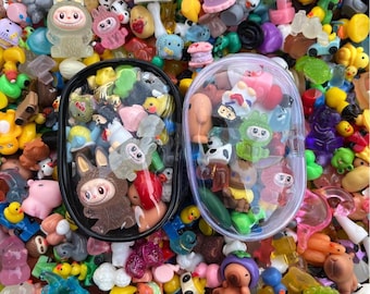 May include: A collection of colorful miniature figurines, including bunnies, animals, and other characters. Two black oval containers hold some of the figurines, while the rest are scattered around. The figurines are in various colors, including pink, yellow, and green.