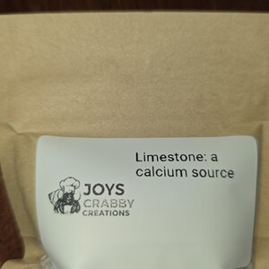 May include: A package of limestone, a calcium source, with the text "Limestone: a calcium source." The package also features a logo with a crab wearing a chef's hat and the text "JOYS CRABBY CREATIONS."