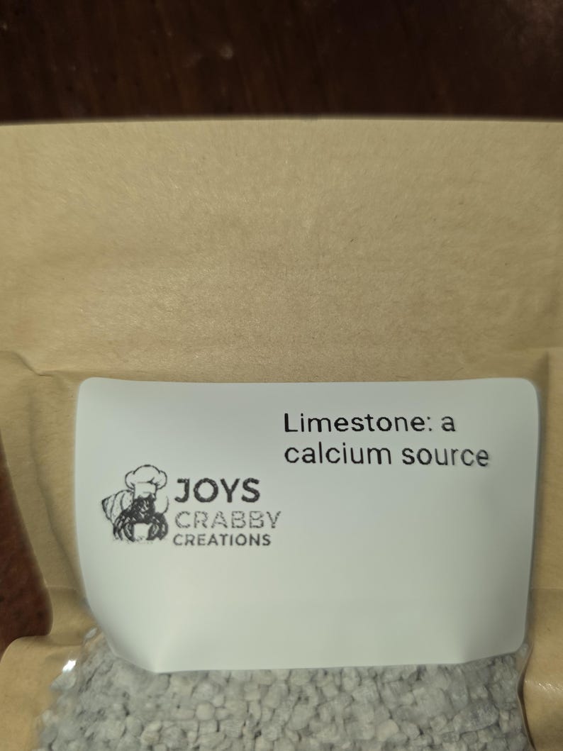 May include: A package of limestone, a calcium source, with the text "Limestone: a calcium source." The package also features a logo with a crab wearing a chef's hat and the text "JOYS CRABBY CREATIONS."