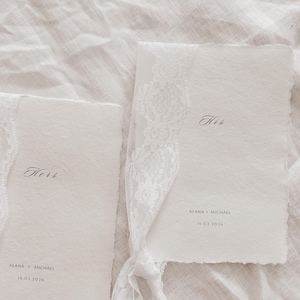 May include: Two white wedding programs with the words "Hers" and "His" in elegant script. The programs are adorned with delicate white lace and tied together. The names "Alana + Michael" and the date "15.02.2016" are printed on the programs.