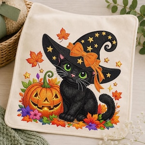 May include: A square off-white fabric item featuring a printed illustration of a black cat wearing a black witch hat with yellow stars and an orange bow. Beside the cat is a carved orange jack-o'-lantern surrounded by colorful autumn leaves.