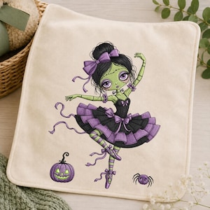 May include: A cream-coloured fabric square featuring an embroidered illustration of a green-skinned ballerina with black hair, a purple bow, and a black and purple tutu. A small purple jack-o'-lantern and a purple spider are embroidered below.