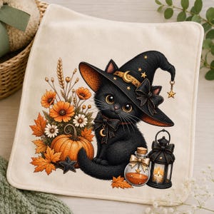 Op de afbeelding: Een vierkante, gebroken witte stoffen doek met een bedrukte illustratie van een zwart kitten met een zwarte heksenhoed met gouden sterren en een maansikkel. Naast het kitten staan oranje bloemen, een pompoen, een glazen flesje en een zwarte lantaarn.