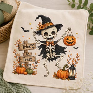 May include: A cream-colored fabric square featuring a printed illustration of a skeleton wearing a witch hat, a cape, and a bow tie. The skeleton holds a jack-o'-lantern. Nearby is a wooden sign reading Trick or Treat, pumpkins, and a lantern.