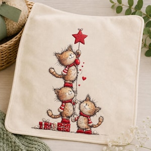 May include: A square off-white fabric cloth featuring a printed illustration of three fluffy brown kittens stacked vertically. The kittens wear red and white striped scarves and red boots. They are holding a red star and red gift boxes.