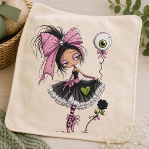 May include: A square off-white fabric piece featuring an embroidered illustration of a character with black hair, a large pink bow with a skull, a black and white tutu with a green heart, pink striped sleeves, and ballet slippers, holding an eyeball balloon.