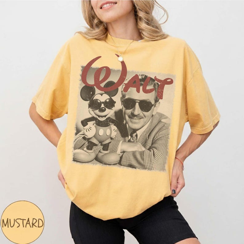 May include: A mustard yellow short-sleeve t-shirt featuring a graphic print of a man in a suit and a cartoon mouse, both wearing sunglasses. The text "Walt" is printed in a large, distressed red font above the figures on the front of the shirt.