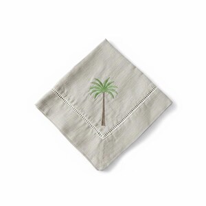 Pode incluir: Uma guardanapo quadrado cinza claro com uma borda vazada branca. O guardanapo apresenta um bordado de palmeira em verde e marrom. O guardanapo &eacute; dobrado em forma de diamante sobre um fundo branco.