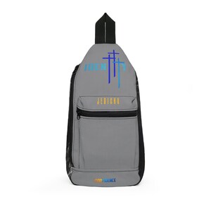 Puede incluir: Bandolera gris con detalles negros y un bolsillo frontal con cremallera. La bolsa presenta la palabra "IDENTITY" sobre tres símbolos de cruz azules y la palabra "JERICHO" en dorado. La palabra "CONFIDENCE" está impresa en la parte inferior.