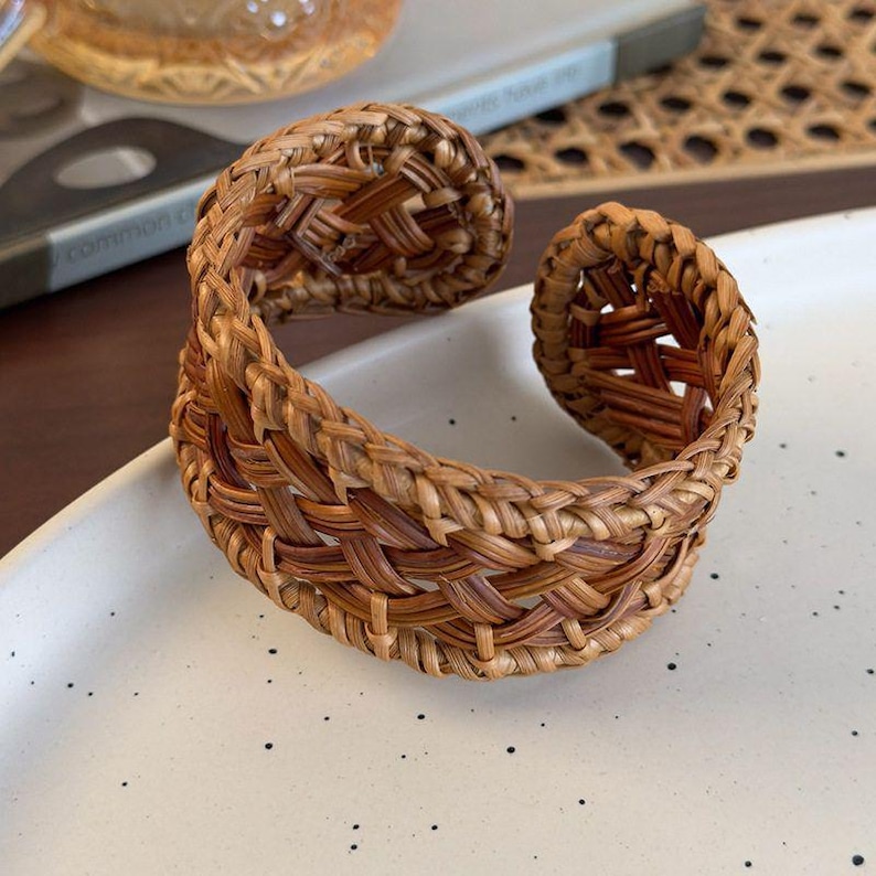 Puede incluir: Una pulsera tipo brazalete trenzada de color marr&oacute;n con un patr&oacute;n de celos&iacute;a abierto e intrincado hecho de fibras vegetales finas y flexibles. La pulsera tiene un dise&ntilde;o circular abierto con bordes redondeados y enrollados.
