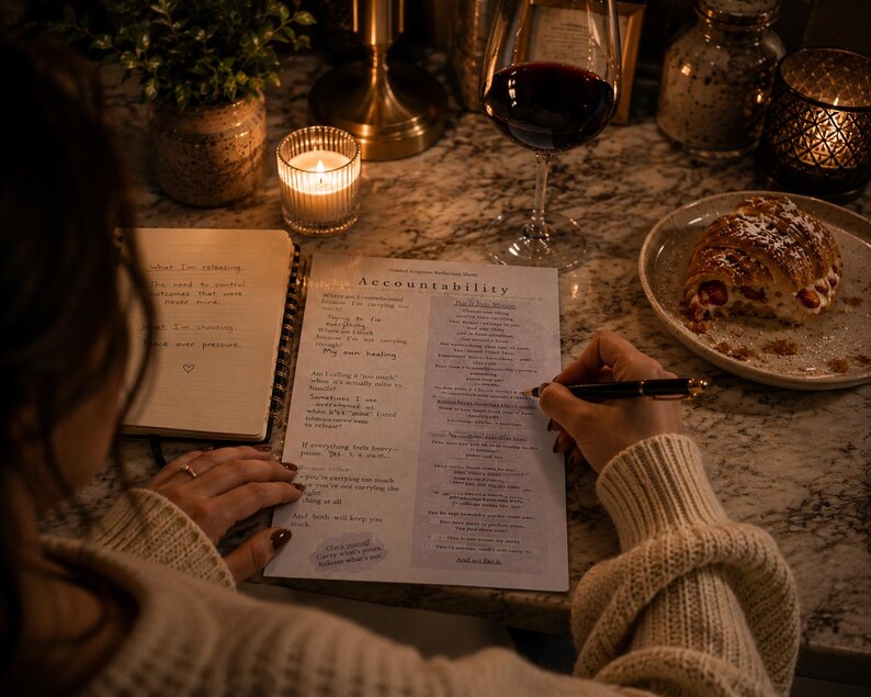 Peut inclure: Une personne &eacute;crit sur une page intitul&eacute;e &laquo;&nbsp;Accountability&nbsp;&raquo; avec un stylo, &agrave; c&ocirc;t&eacute; d'un cahier. Un verre de vin rouge et une assiette avec une p&acirc;tisserie sont &eacute;galement sur la table. Une bougie allum&eacute;e et une petite plante sont en arri&egrave;re-plan.
