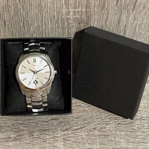 Puede incluir: Un reloj Fossil plateado con esfera clara y agujas negras, presentado en una caja negra. El reloj tiene una correa plateada con detalles negros. La esfera del reloj tiene el logotipo de Fossil y la palabra "water resistant".