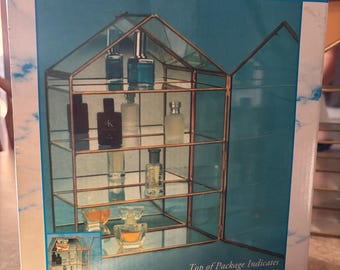 Puede incluir: Una caja de producto para un Fragrance & Curio Cabinet que muestra una vitrina de cristal con forma de casa y marco de metal cobrizo. La caja incluye el texto "Fragrance & Curio Cabinet", "Top of Package Indicates Which Cabinet is Inside" y "Comes in Two Styles: Octagon or House Shape."