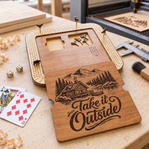 May include: A wooden cribbage board with a removable lid featuring a laser-engraved cabin, mountain, and forest scene with the text "Take it Outside." The board includes small animal-shaped metal pegs, a grid of holes, and a storage compartment.