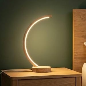 Peut inclure: Une table de chevet en bois avec une lampe en forme de croissant émettant une lumière chaude. La lampe est posée sur la table de chevet, à côté d'un lit avec une tête de lit en bois. L'ensemble est dans une chambre.