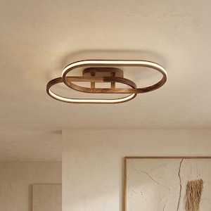May include: A ceiling light fixture featuring two overlapping oval-shaped wooden frames with integrated LED light strips that emit a warm glow. The structure is mounted to the ceiling and showcases a natural wood grain finish throughout the design.