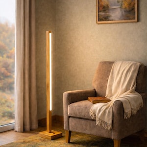 May include: A tall, slender floor lamp featuring a vertical light strip embedded within a light-toned wooden post. The lamp stands on a square wooden base and emits a warm, bright glow, illuminating the surrounding area with a soft, vertical beam.