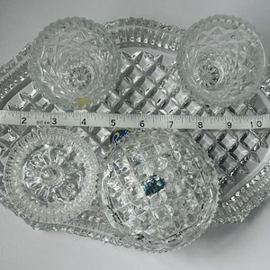 May include: A clear, cut-glass serving set with a tray, two small bowls, two candle holders, and a round dish. The tray measures approximately 12 inches long. The set has a diamond pattern.