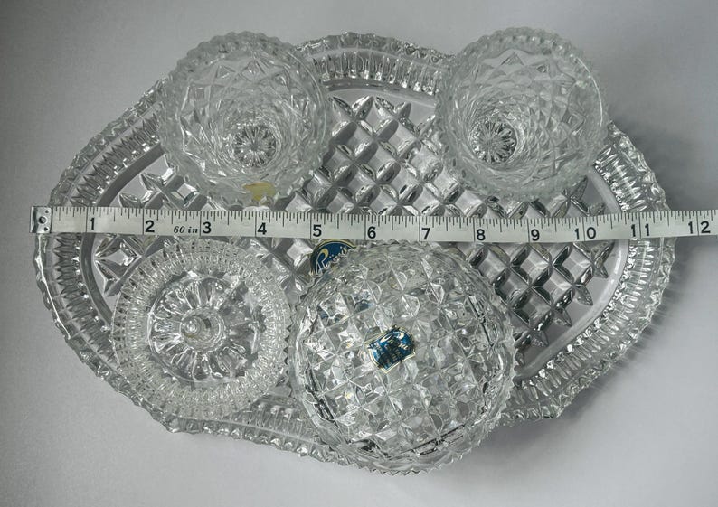 May include: A clear, cut-glass serving set with a tray, two small bowls, two candle holders, and a round dish. The tray measures approximately 12 inches long. The set has a diamond pattern.