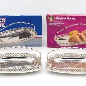 Peut inclure: Deux plateaux rectangulaires argentés avec des anses en fil torsadé et des côtés en treillis décoratif. Chaque plateau est accompagné de son emballage d'origine, une boîte bleue marquée Queen Anne et une boîte rose marquée Queen Anne Silver Plated Sandwich Tray.