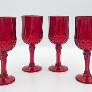 Op de afbeelding: Een set van vier bijpassende rode glazen kelken met een ruitpatroon op de onderkant van de kelk en een gefacetteerd steeltje. Elk glas heeft een ronde voet en een gladde, heldere rand, uitgevoerd in een dieprode kleur.