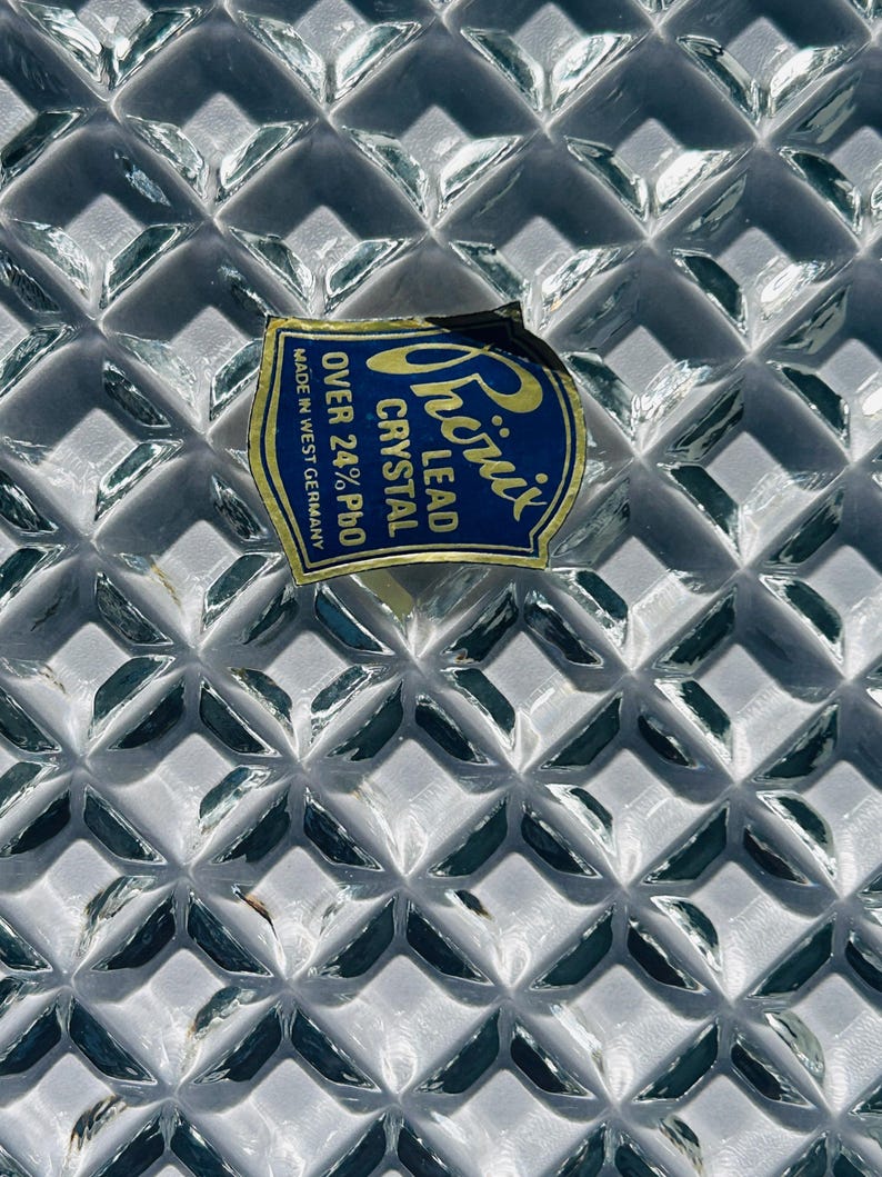 May include: Close-up of a clear lead crystal glass with a diamond pattern. A blue and yellow label reads "Phoenix Lead Crystal Over 24% PbO Made in West Germany."
