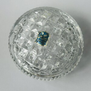 May include: Clear lead crystal bowl with a diamond pattern. The bowl has a scalloped edge and a blue and gold label that reads "Lead Crystal Over 24% Pbo".