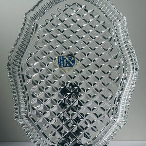 May include: Clear lead crystal serving tray with a diamond pattern and scalloped edges. The tray has a blue and white label that reads "Phoenix Crystal Over 24% Pbo". The tray is displayed on a black metal stand.