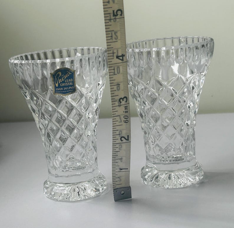 May include: Two clear lead crystal vases with a diamond pattern, each approximately 4 inches tall. A measuring tape is placed next to the vases. One vase has a blue and white label that reads "Phoenix Lead Crystal Over 24% PbO".
