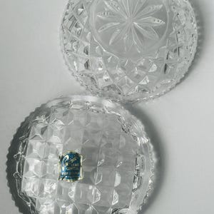 May include: Two clear, cut-glass bowls with diamond and starburst patterns. One bowl has a label that reads "Lead Crystal Over 24% Pbo". The bowls are round with a scalloped edge, and are likely decorative or serving pieces.