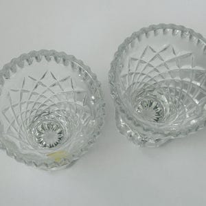 May include: Two clear, cut-glass bowls with a diamond pattern and scalloped rims. The bowls have a pedestal base and a spiral design leading to the center. The glass reflects light, creating a sparkling effect. These bowls are suitable for serving small portions.