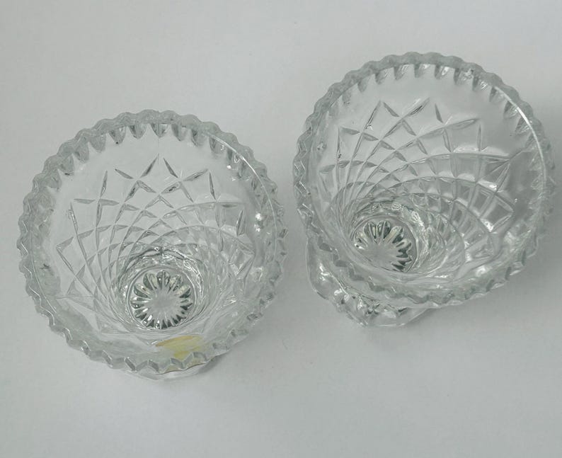 May include: Two clear, cut-glass bowls with a diamond pattern and scalloped rims. The bowls have a pedestal base and a spiral design leading to the center. The glass reflects light, creating a sparkling effect. These bowls are suitable for serving small portions.