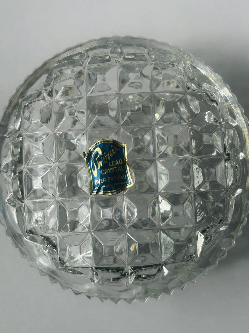 May include: Clear lead crystal bowl with a diamond pattern. The bowl has a rounded shape and a textured surface. A blue and gold label is affixed to the bowl, indicating it is lead crystal.