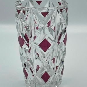May include: A clear glass vase featuring a geometric diamond-cut pattern with alternating deep magenta-coloured diamond insets. The cylindrical vessel has a faceted surface texture and a thick, sturdy base with a scalloped edge design.