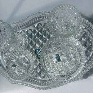 May include: A clear, cut-glass serving set with a tray and three dishes. The tray has a diamond pattern and a scalloped edge. The dishes have a variety of cut glass patterns. A blue and white label is visible.