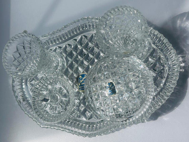 May include: A clear, cut-glass serving set with a tray and three dishes. The tray has a diamond pattern and a scalloped edge. The dishes have a variety of cut glass patterns. A blue and white label is visible.