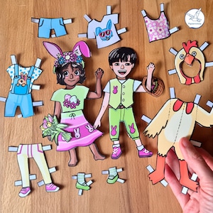 Könnte beinhalten: Papierpuppen mit Outfits zum Thema Ostern, darunter Hasenohren, Latzhosen und ein Hühnerkostüm. Die Puppen sind in Pastellfarben mit Blumen- und Hasenmustern gekleidet. Ein Blumenstrauß wird von einer der Puppen gehalten.