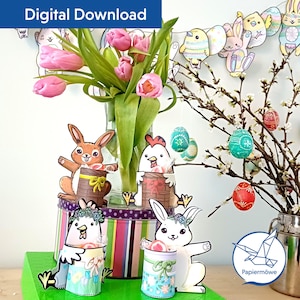 Könnte beinhalten: Eine Osterdekoration mit Papierschnitten von Hasen und einem Huhn, die dekorative Behälter halten. Rosa Tulpen in einer Glasvase und hängende Ostereier ergänzen die festliche Szene. Der Text "Digital Download" befindet sich in einem blauen Rechteck.