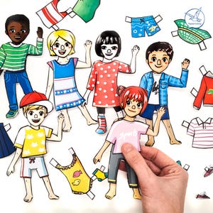Könnte beinhalten: Eine Sammlung von Papierpuppen und Kleidungsausschnitten. Die Puppen haben unterschiedliche Hauttöne, Frisuren und Outfits. Die Kleidung umfasst Hemden, Shorts, Kleider und Accessoires. Eine Hand hält eine Puppe mit einem rosa Shirt mit dem Wort "Sport".