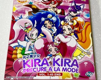 Puede incluir: Una caja de DVD rectangular con una colorida ilustración de anime de seis personajes con cabello y atuendos vibrantes. La portada muestra el texto KIRA KIRA PRECURE A LA MODE VOL. 1-49 END en morado y blanco sobre un fondo rosa con estrellas.