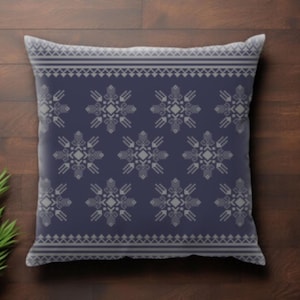 May include: A square decorative pillow with a navy blue background and a repeating gray geometric pattern. The pattern includes stylized floral and geometric shapes. The pillow is placed on a wooden surface with a green plant in the corner.