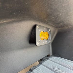 May include: A black metal LED light fixture with a yellow lens is mounted on a dark surface. The fixture is secured with silver screws and has the text "S PRO" printed on it. The light is designed for automotive use.