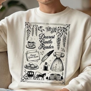 May include: Cream-colored sweatshirt with a black and white graphic that reads "Dearest Gentle Reader." The graphic includes a teacup, feather, dress, and carriage. The person is wearing ripped blue jeans.