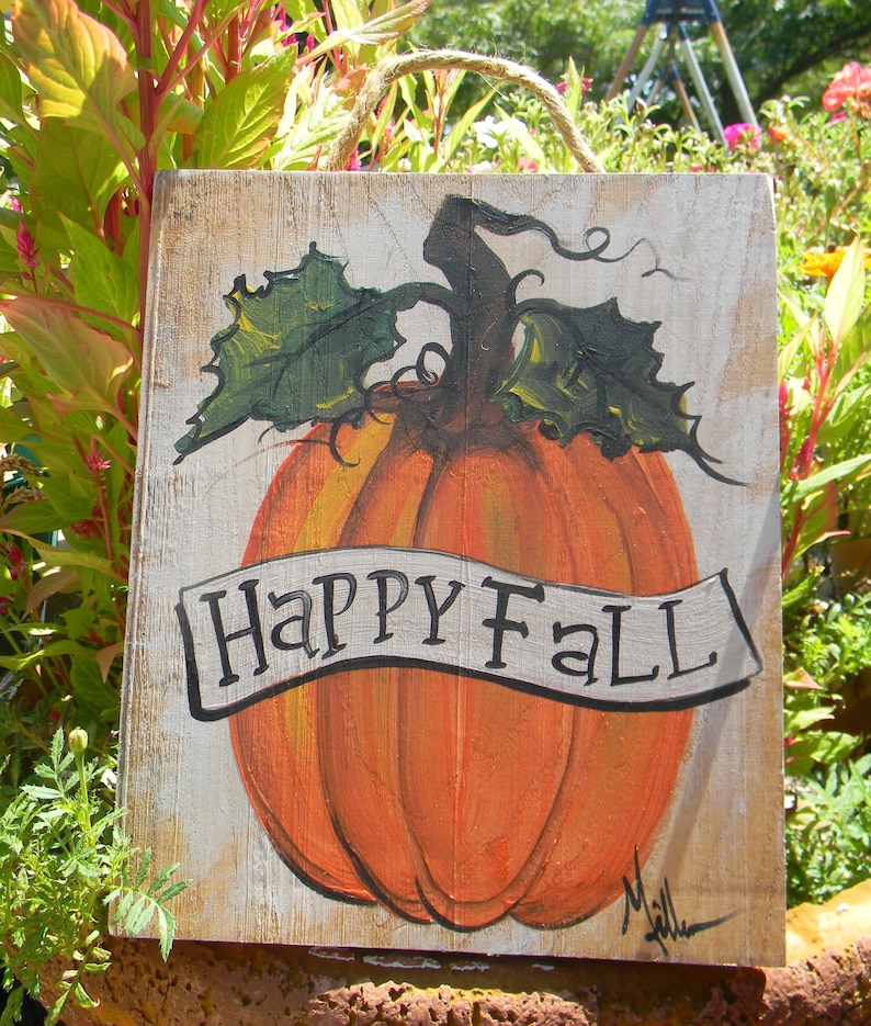 May include: A wooden sign with a painted pumpkin and the words "Happy Fall" in a white banner. The pumpkin is orange with green leaves and a brown stem.