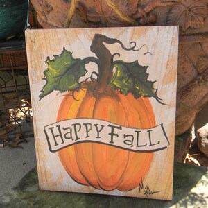 May include: A wooden sign with a painted orange pumpkin and green leaves. The sign says "Happy Fall" in a white banner.