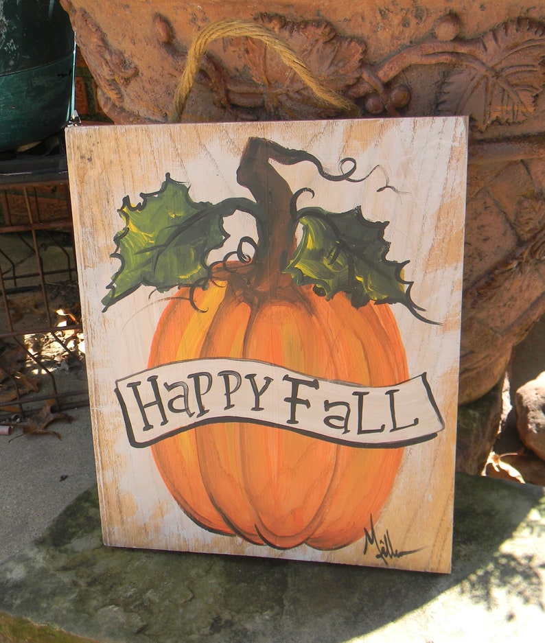 May include: A wooden sign with a painted orange pumpkin and green leaves. The sign says "Happy Fall" in a white banner.