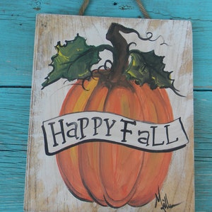 May include: A hand-painted wooden sign with a white background features a large orange pumpkin with green leaves and a brown stem. The pumpkin has a white banner that reads "Happy Fall".
