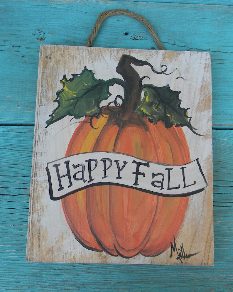 May include: A hand-painted wooden sign with a white background features a large orange pumpkin with green leaves and a brown stem. The pumpkin has a white banner that reads "Happy Fall".